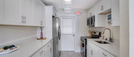 A modern kitchen with white cabinets, stainless steel appliances, and a blue rug.
