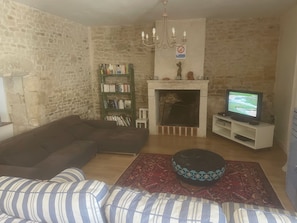 Una sala de estar con pared de piedra, chimenea, televisor, estantería y sofá a rayas.