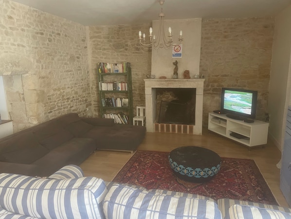 Een woonkamer met een stenen muur, een open haard, een televisie, een boekenkast en een gestreept bankje.