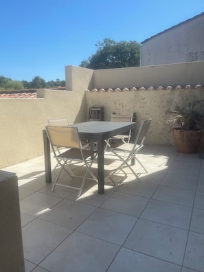 Een terras buiten met een tafel, stoelen, een potplant en een betegelde vloer.