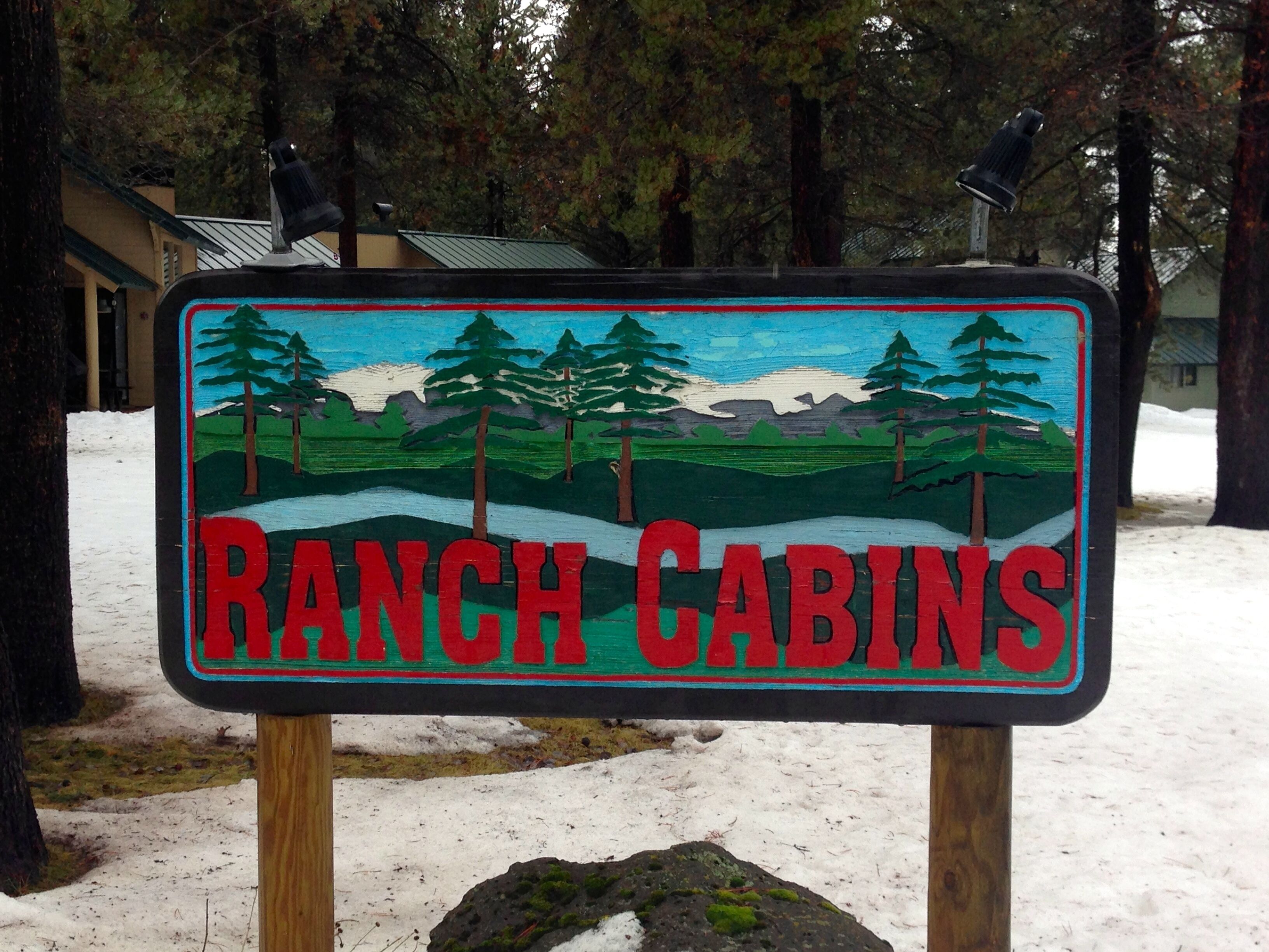 A sign for 'Ranch Cabins' with a painted landscape of trees and mountains.