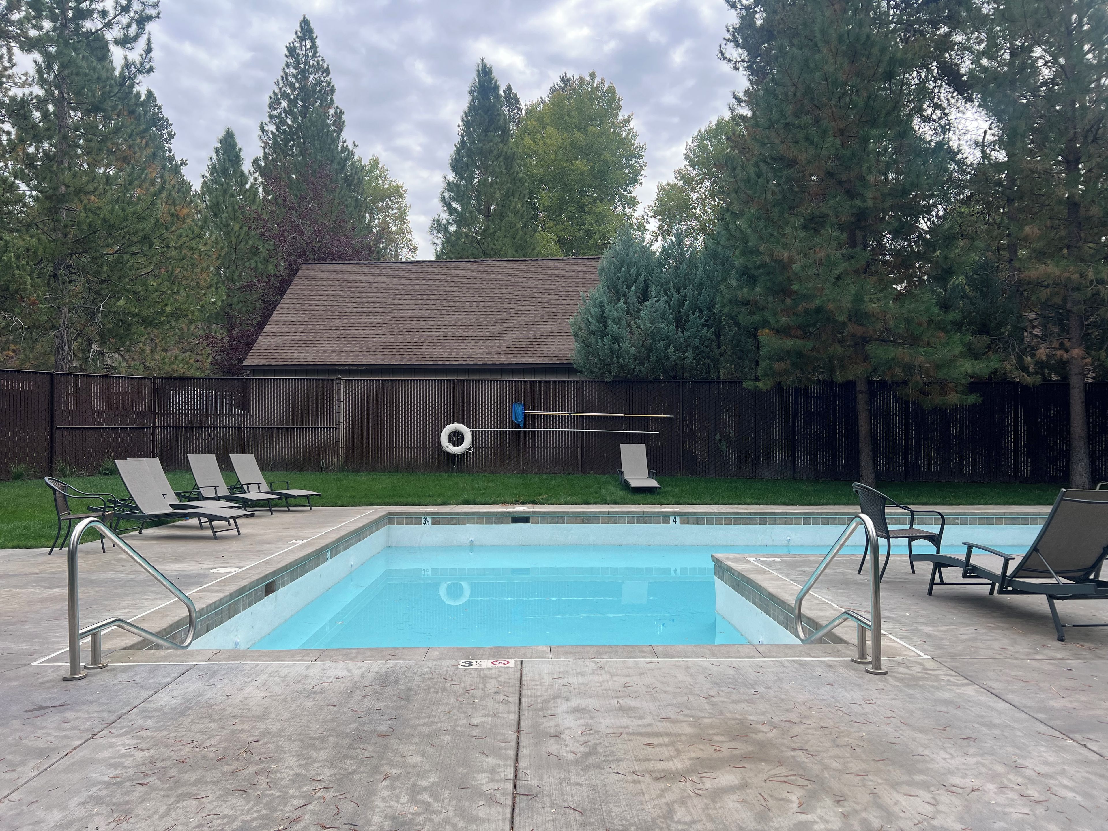 A rectangular swimming pool with a tiled edge, surrounded by lounge chairs and a metal ladder.