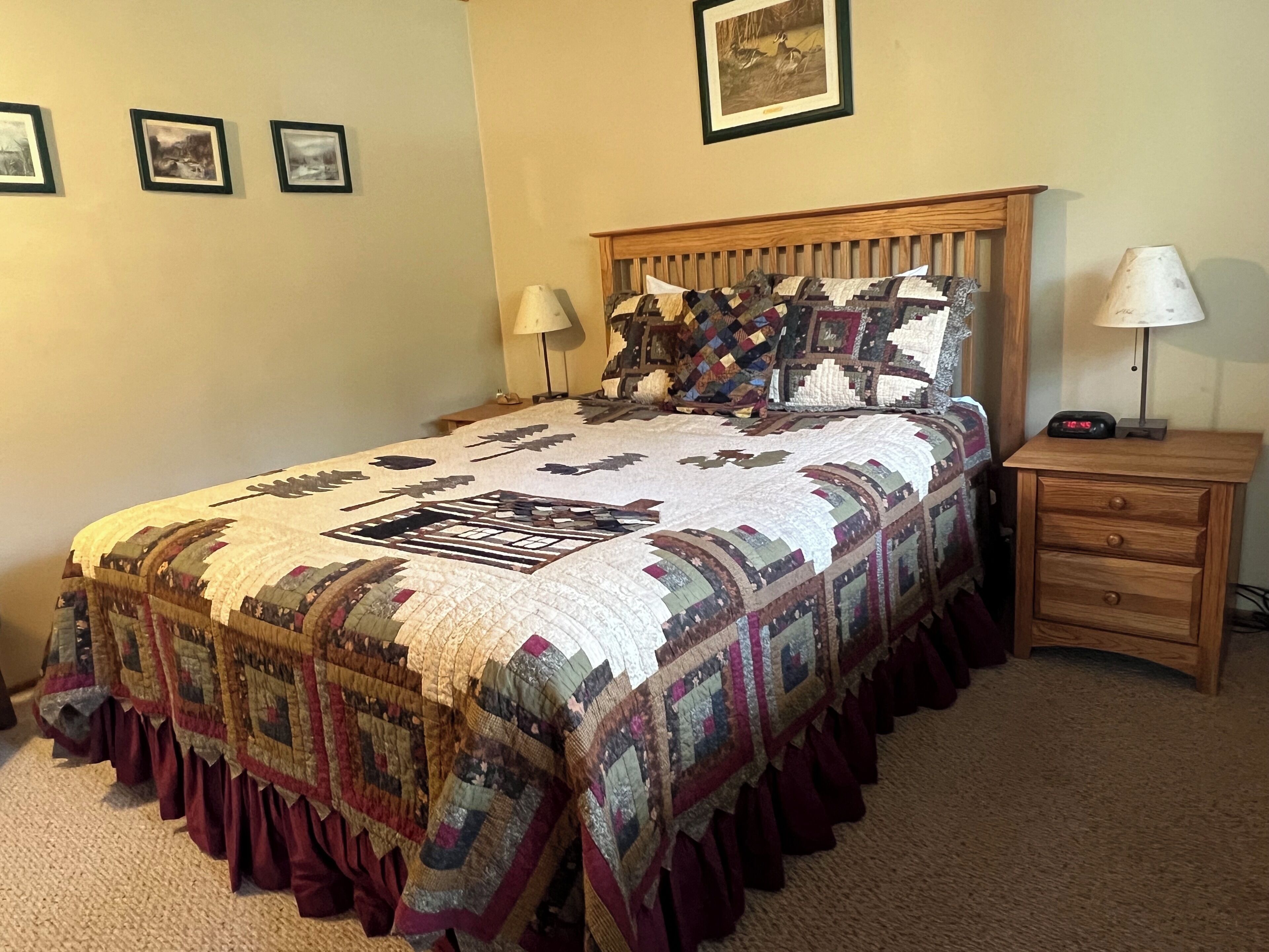 A bedroom with a large bed, a wooden nightstand, a lamp, and framed pictures on the wall.