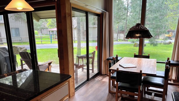Une cuisine moderne dotée d’un grand îlot central, d’un coin repas avec des chaises et une table en bois, et d’une porte-fenêtre coulissante donnant sur un jardin avec une pelouse et une terrasse en bois.