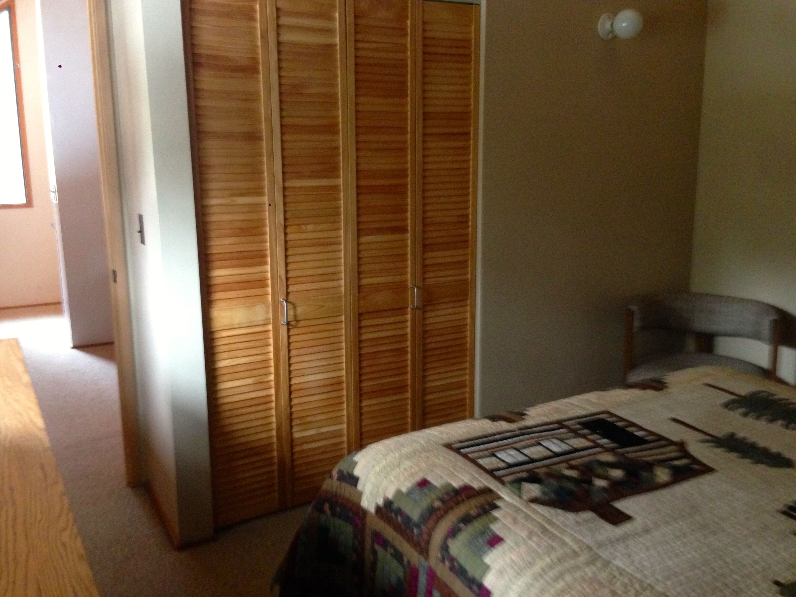 Un dormitorio con un armario de madera, una cama con colcha y una silla.