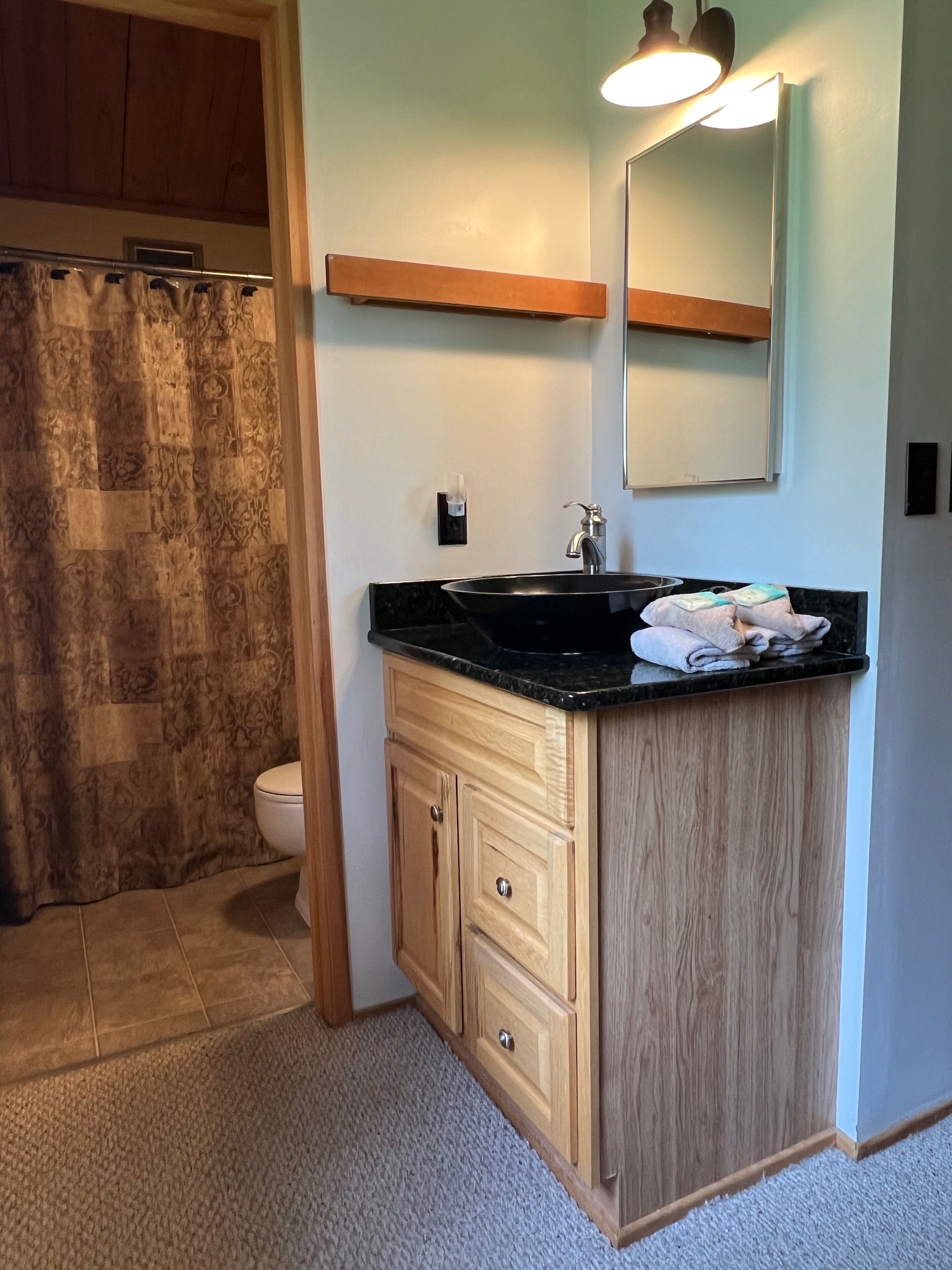 A bathroom with a black sink, wooden cabinets, a mirror, and a towel rack.