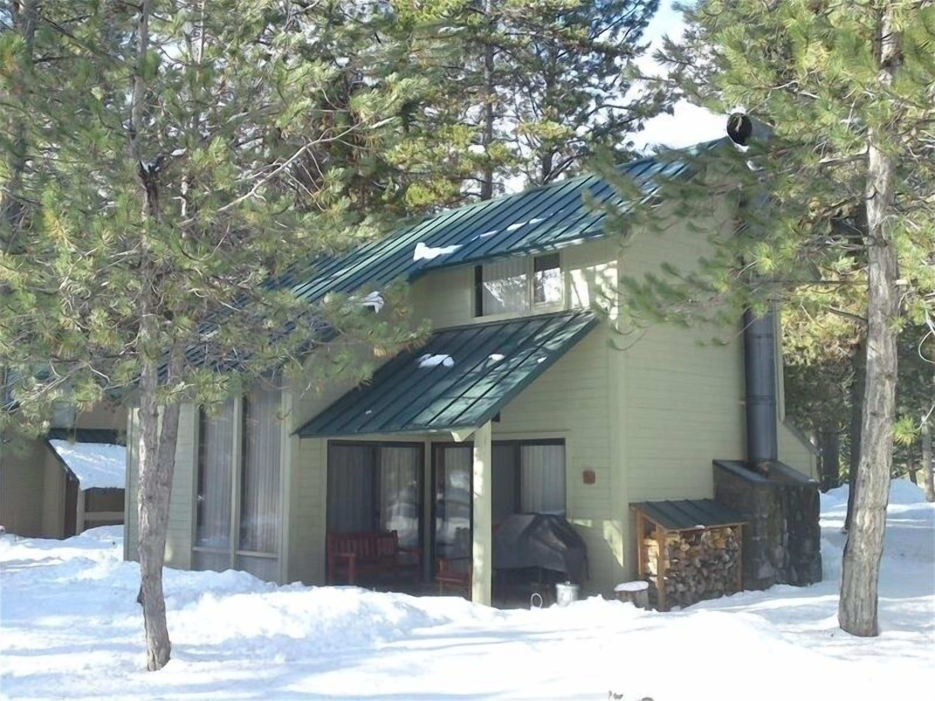 A small, single-story building with a sloped roof, surrounded by trees and covered in snow.