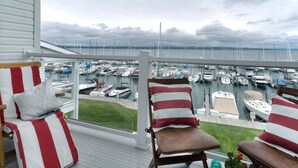 Un balcón con dos sillas a rayas, una mesita y vista a un puerto deportivo con barcos.