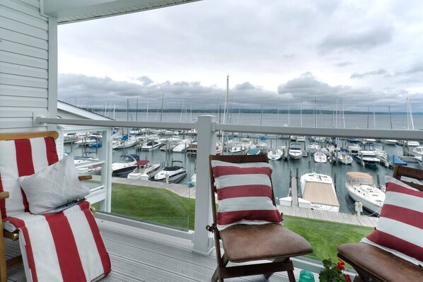 A balcony with two striped chairs, a small table, and a view of a marina with boats.