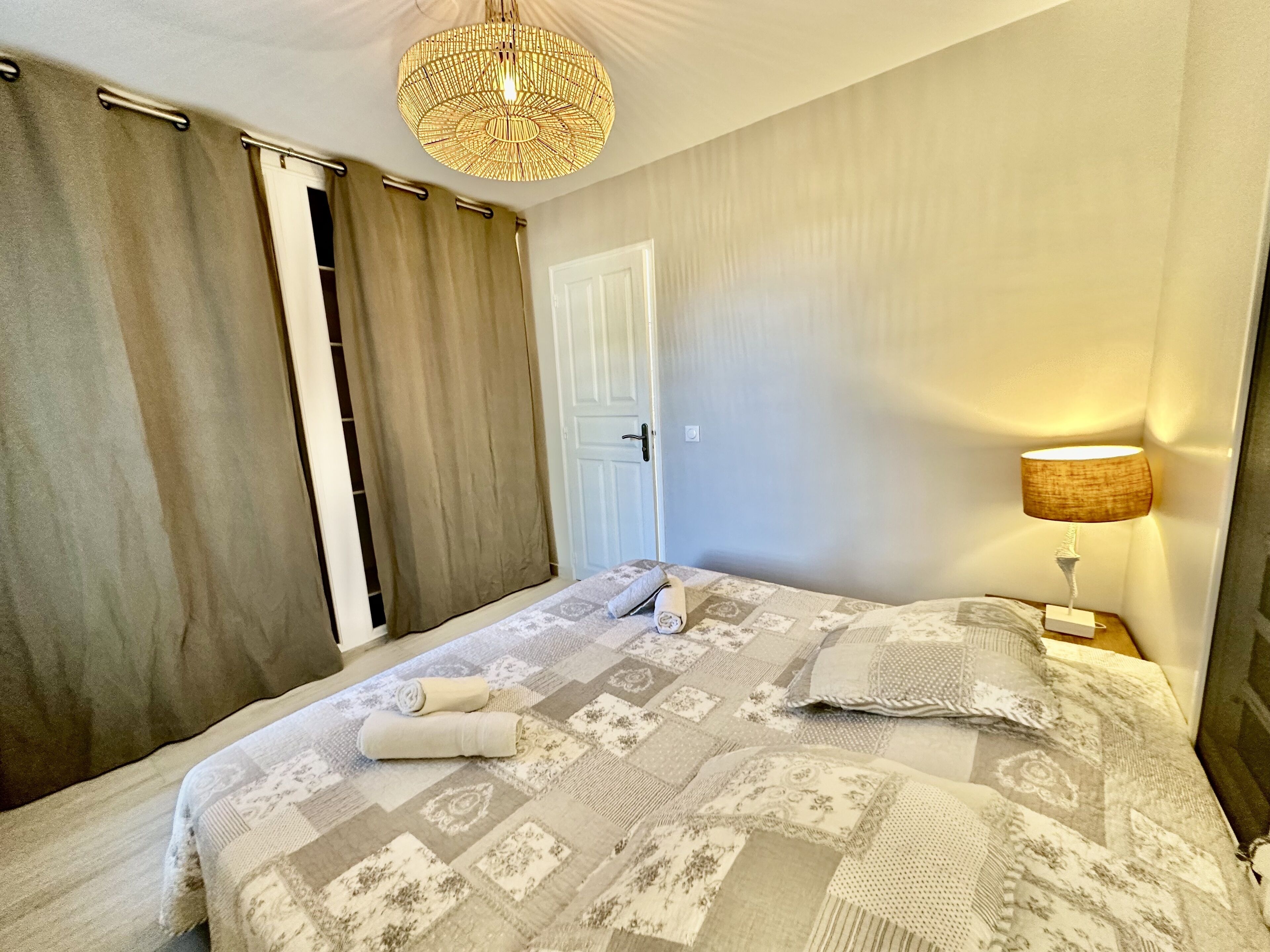 Quarto com cama, luminária de cabeceira, porta e janela com cortinas.