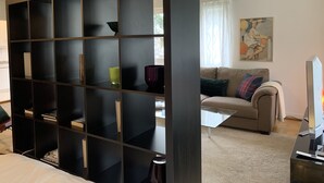 A modern living room with a dark wooden bookshelf, a beige sofa, a glass coffee table, and a flat-screen TV. - Large charming apartment, bright, close to the center and the Old Town (Genève)