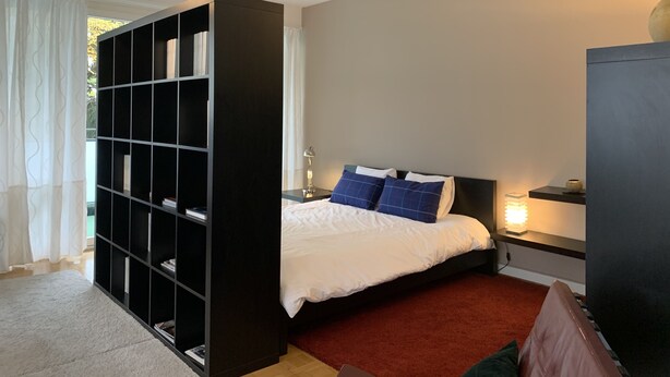 A bedroom with a bed, a bookshelf, a desk with a lamp, and a nightstand with a lamp. - Large charming apartment, bright, close to the center and the Old Town (Genève)