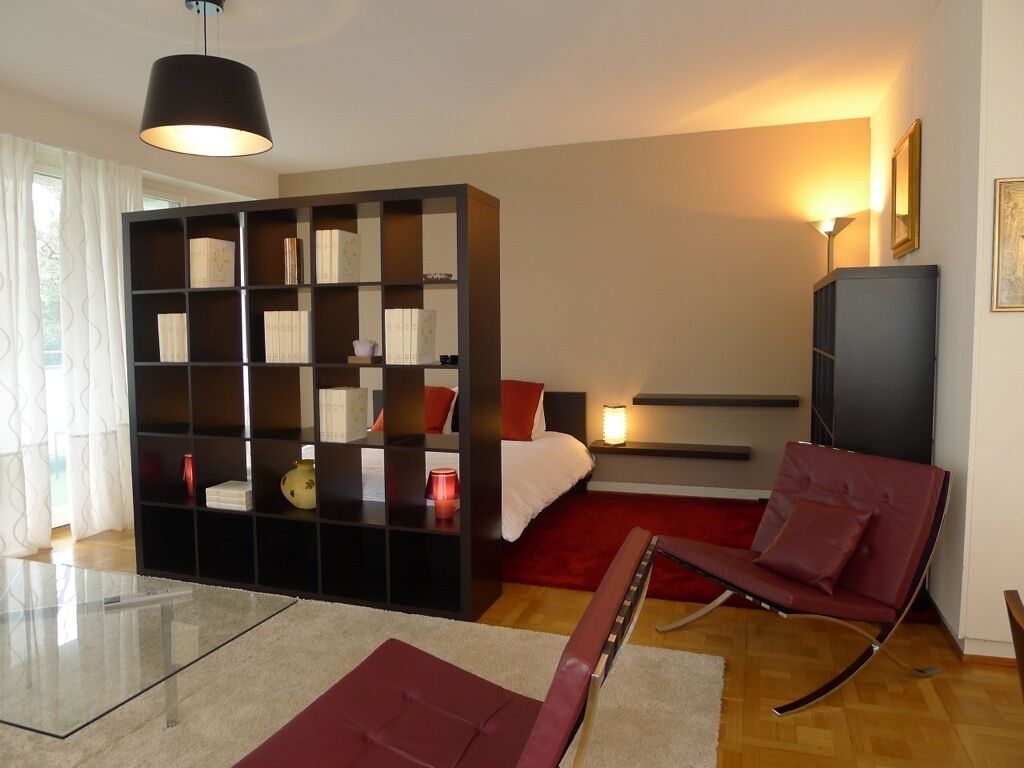 Ein modernes Schlafzimmer mit einer großen, schwarzen Regaleinheit, einem roten Sofa, einem Glastisch und einem Bett mit roter Kopfteil.