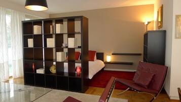Ein modernes Schlafzimmer mit einer großen, schwarzen Regaleinheit, einem roten Sofa, einem Glastisch und einem Bett mit roter Kopfteil.