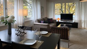 A modern living room with a sofa, a TV, a dining table with plates and glasses, and a vase with flowers. - Large charming apartment, bright, close to the center and the Old Town (Genève)