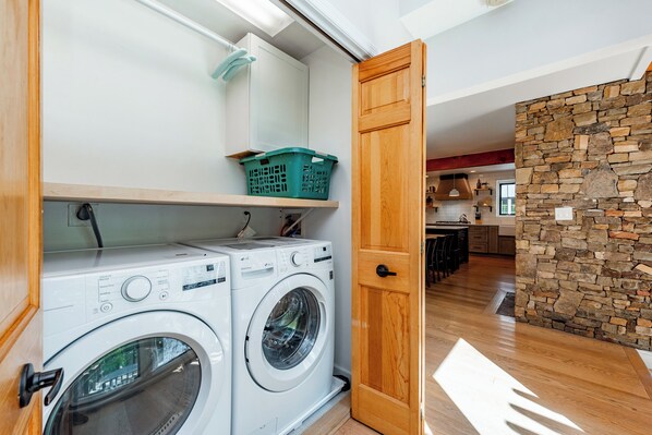 A laundry area with two front-loading washing machines, a wooden door, and a stone wall. - Sleek Mountain Luxury Home w/ Dock Slip & Fire Pit (Oakland)