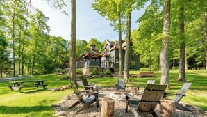 Een chalet met een vuurplaats van natuursteen, omgeven door een natuurlijke omgeving met bomen en een picknicktafel.