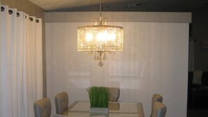 A dining area with a glass table, six grey upholstered chairs, a chandelier, and a potted plant. - Elegant Las Vegas rental (Las Vegas)
