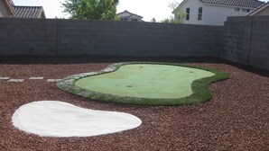 A backyard with a small artificial green area and a white patch, surrounded by a brick wall and pebbles. - Elegant Las Vegas rental (Las Vegas)