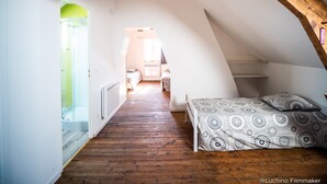 Un dormitorio bajo y con techo inclinado, con vigas de madera, una cama con ropa de cama estampada y vistas a otra habitación.