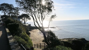 Un sendero costero con cerca de madera que lleva a una playa, con vista al mar y cielo despejado.