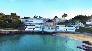 Un hotel costero con una gran edificación que domina el mar, una playa y un jardín ajardinado.