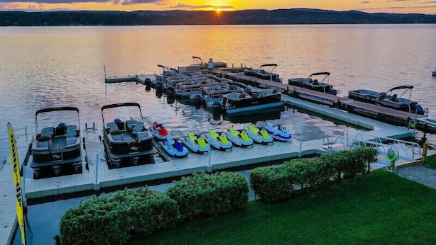 A marina with boats docked at the pier, surrounded by water and a sunset in the background. - Cozy Boat House Lake Charlevoix: Amazing View/Pool (Charlevoix)