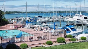 A marina with boats docked, a swimming pool with lounge chairs, and a view of the water. - Cozy Boat House Lake Charlevoix: Amazing View/Pool (Charlevoix)