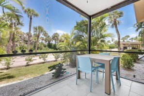 Un balcon avec une table et des chaises, donnant sur un jardin agrémenté de palmiers et offrant une vue sur un ciel dégagé.