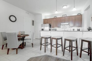 A modern kitchen with white cabinets, stainless steel appliances, and a dining area with a white table and chairs.