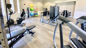 Un gimnasio con varios equipos de ejercicio, incluyendo cintas de correr, una prensa de banca y pesas sueltas.