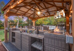 An outdoor bar area with wicker furniture, a fire feature, and string lights.