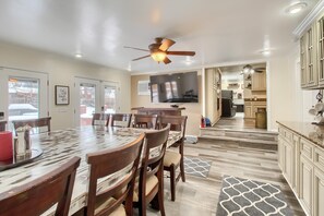 A spacious dining area with a large wooden table and chairs, a ceiling fan, and a television mounted on the wall.