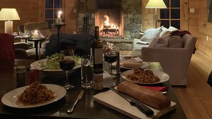A cozy cabin interior with a fireplace, wooden walls, a dining table with food, and a chandelier. - Cabin With A View (Burnsville)