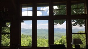 A room with large windows offering a view of a forested landscape and mountains. - Cabin With A View (Burnsville)