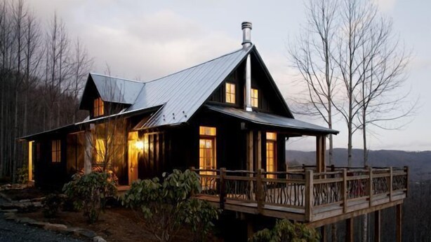 A rustic cabin with a wooden deck and a metal roof, surrounded by trees. - Cabin With A View (Burnsville)