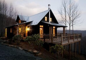 Un chalet rustique doté d’une terrasse en bois et d’un toit en métal, entouré d’arbres.