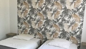 A room with two beds, each with a grey quilted bedspread and white pillows. The headboard features a tropical leaf pattern. - House 4 km from Cargese. (Cargèse)