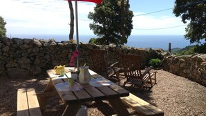 A wooden picnic table with a stone wall backdrop, a red umbrella, and a view of the sea. - House 4 km from Cargese. (Cargèse)