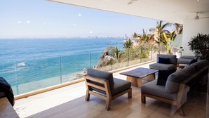 Una sala de estar moderna con vista al océano, que incluye un sofá, sillas y una mesa de centro.