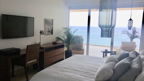 Un dormitorio con una cama grande, un escritorio, una silla, un televisor y vista al océano.