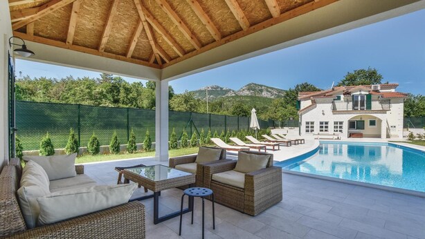A covered outdoor area with wicker furniture, a pool, and a view of a house with a pool. - Luxurious home in Hrvace (Hrvace)