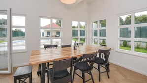 A spacious dining area with a wooden table and black chairs, large windows offering a view of a house and greenery. - Luxurious home in Hrvace (Hrvace)