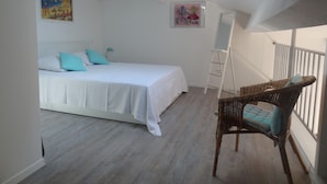 A bedroom with a bed, a standing desk, a wicker chair, and artwork on the walls.