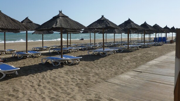 Een strand met rijen ligbedden en rieten parasols.