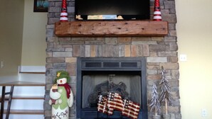 A fireplace with a flat-screen TV above it, flanked by two red and white striped Christmas stockings. - Bellawood Resort #1 Lakefront Cabin with Boat Slip - Unobstructed View! (Greers Ferry)