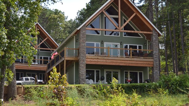 A two-story lodge with a balcony and a covered deck, surrounded by trees. - Bellawood Resort #1 Lakefront Cabin with Boat Slip - Unobstructed View! (Greers Ferry)