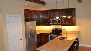 A kitchen with wooden cabinets, a stainless steel refrigerator, a built-in oven, a granite countertop, and pendant lighting. - Bellawood Resort #1 Lakefront Cabin with Boat Slip - Unobstructed View! (Greers Ferry)