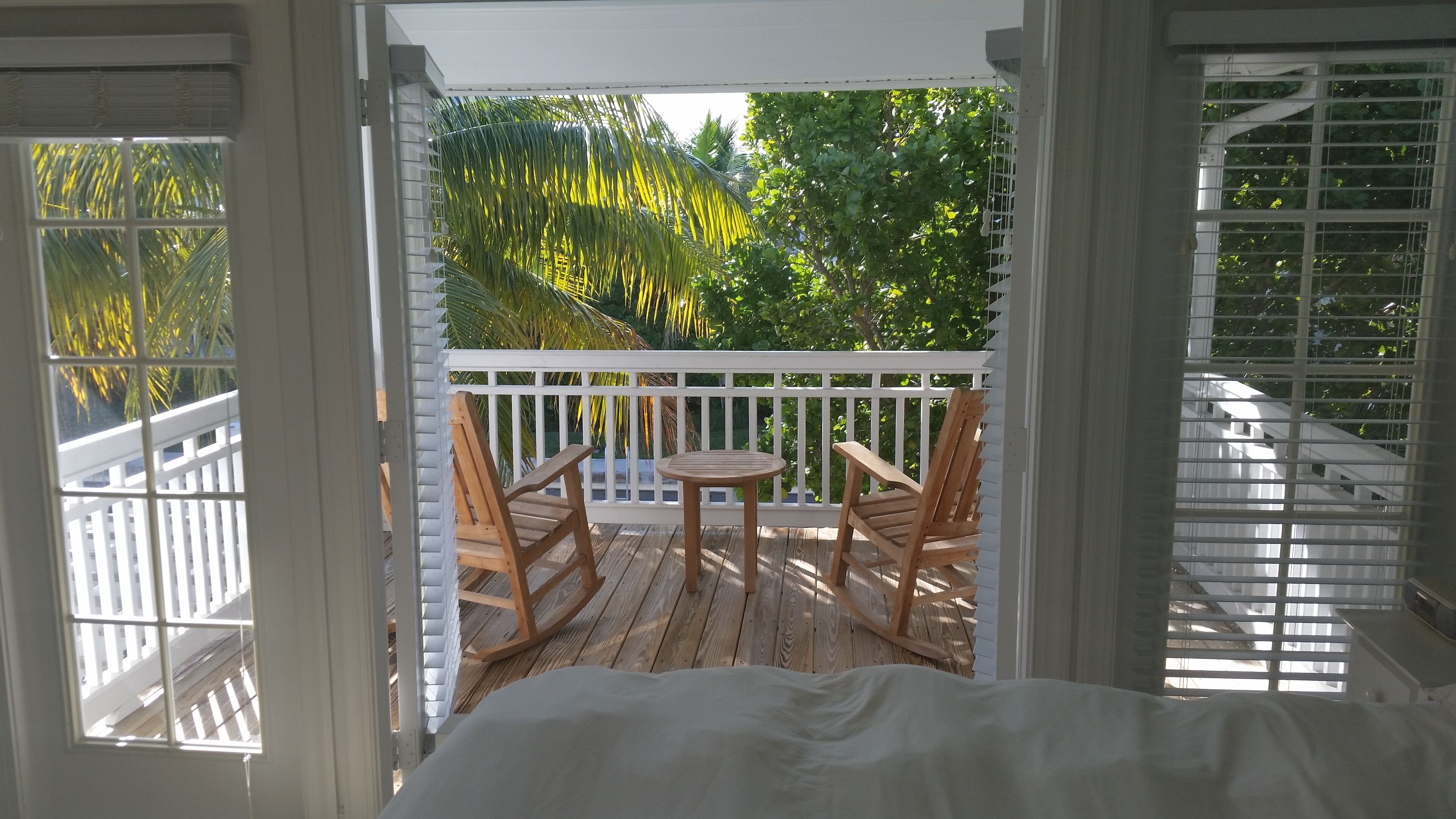 A balcony with a wooden deck, two wooden chairs, and a small round table.