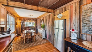 Una cocina rústica con paredes de madera, un refrigerador de acero inoxidable y un comedor con mesa y sillas de madera.